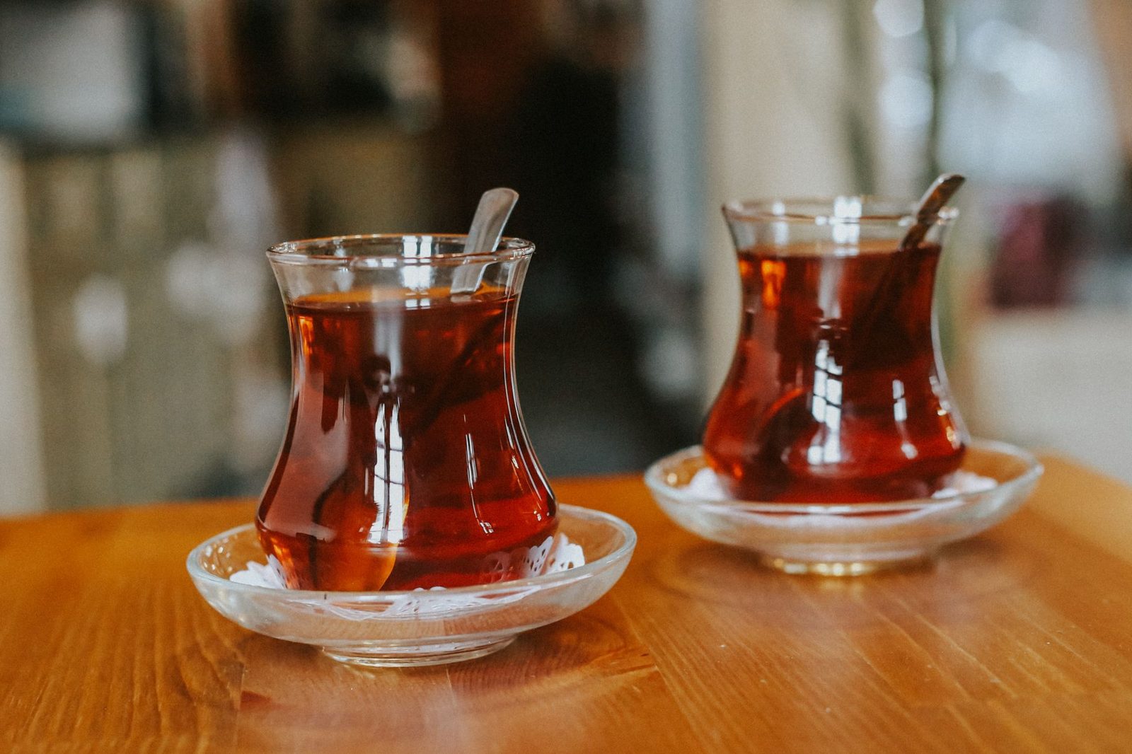 Ahşap masada ince belli bardaklarda servis edilmiş iki çay — yakın aile sohbetinin sade temsili