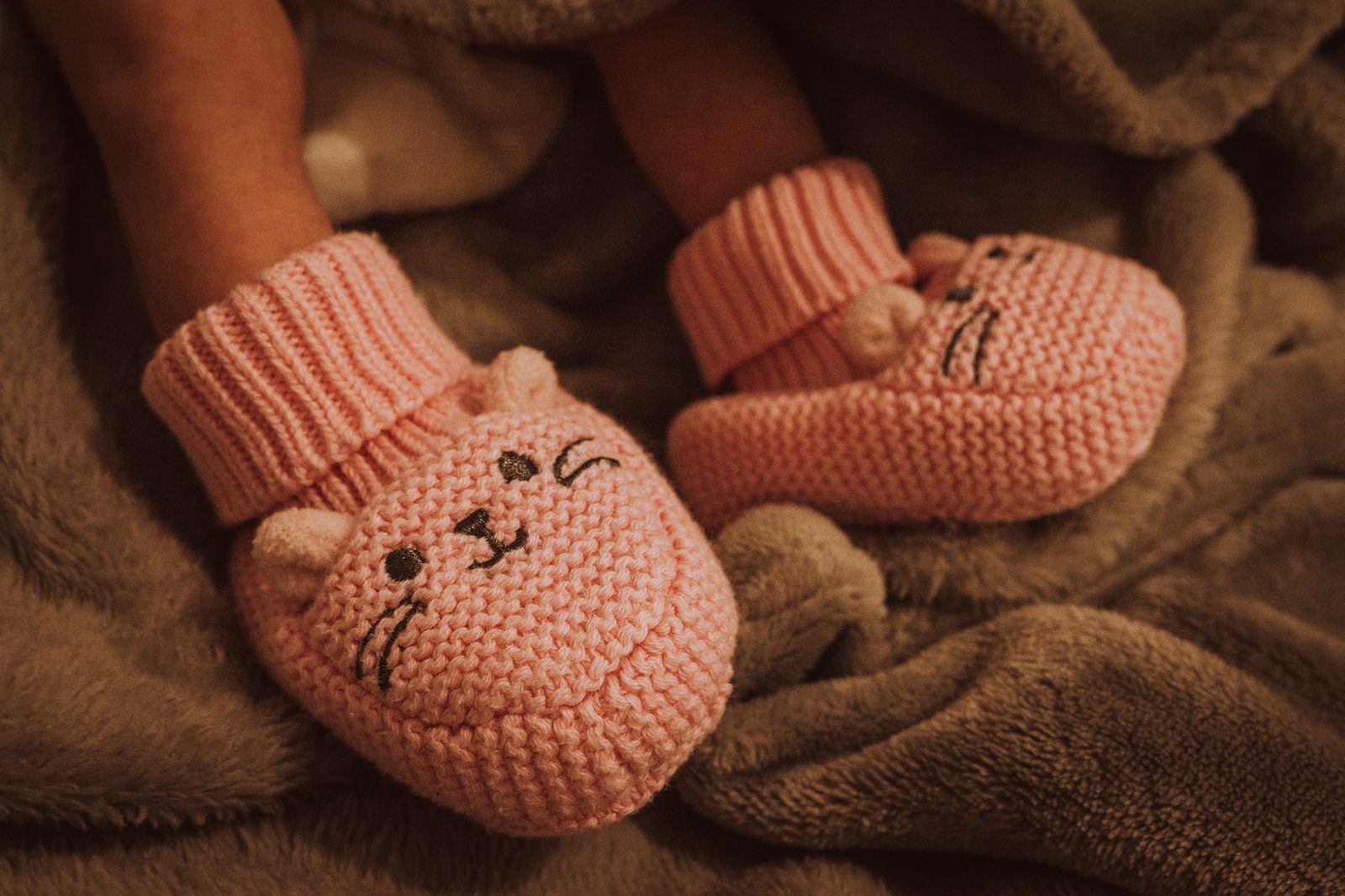 Yumuşak bir battaniyenin üzerinde duran pembe örgü bebek patikleri