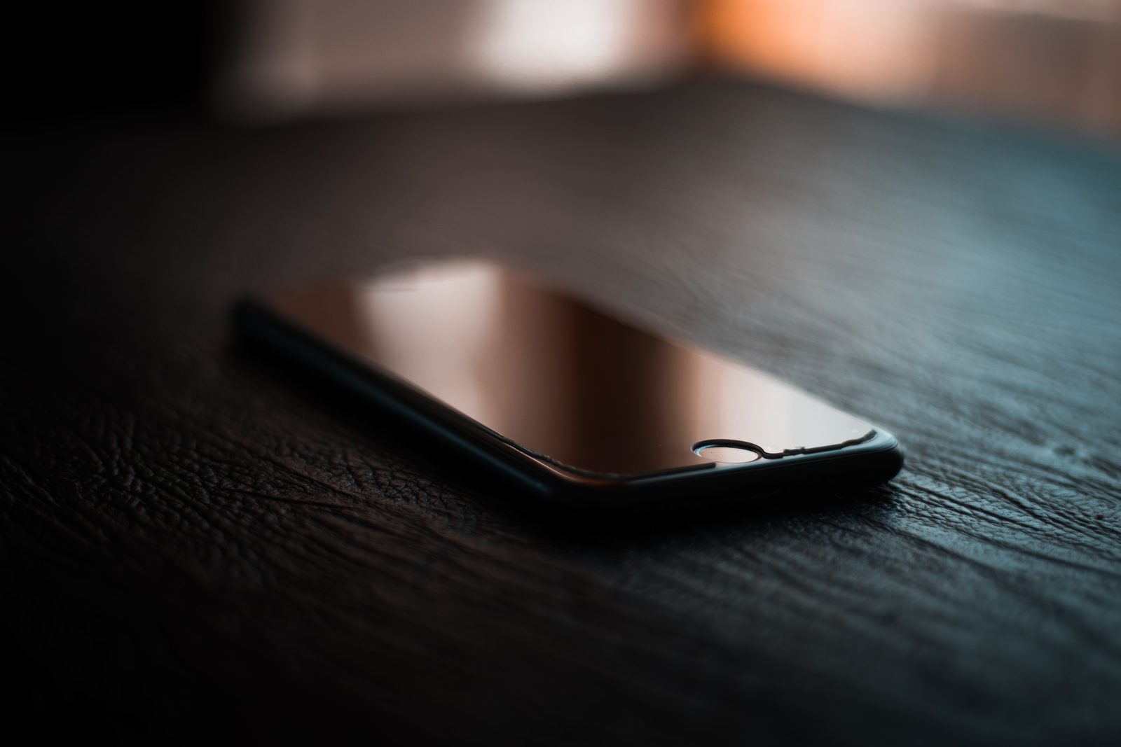 Loş ışıkta ahşap masanın üzerinde ekranı kapalı duran bir cep telefonu