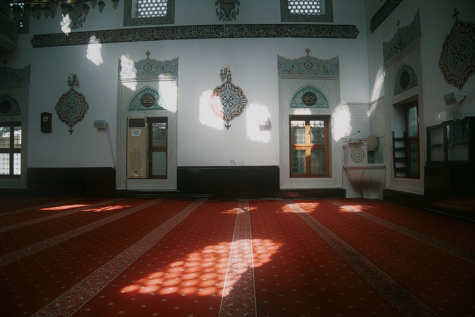 Güneş ışığının halıya desen düşürdüğü boş bir cami iç mekânı