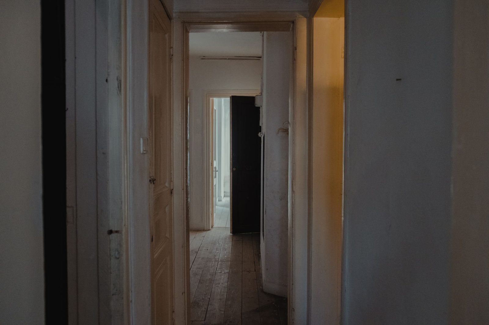 Ahşap kapıları olan, gündüz ışığında loş kalmış sıradan bir apartman koridoru
