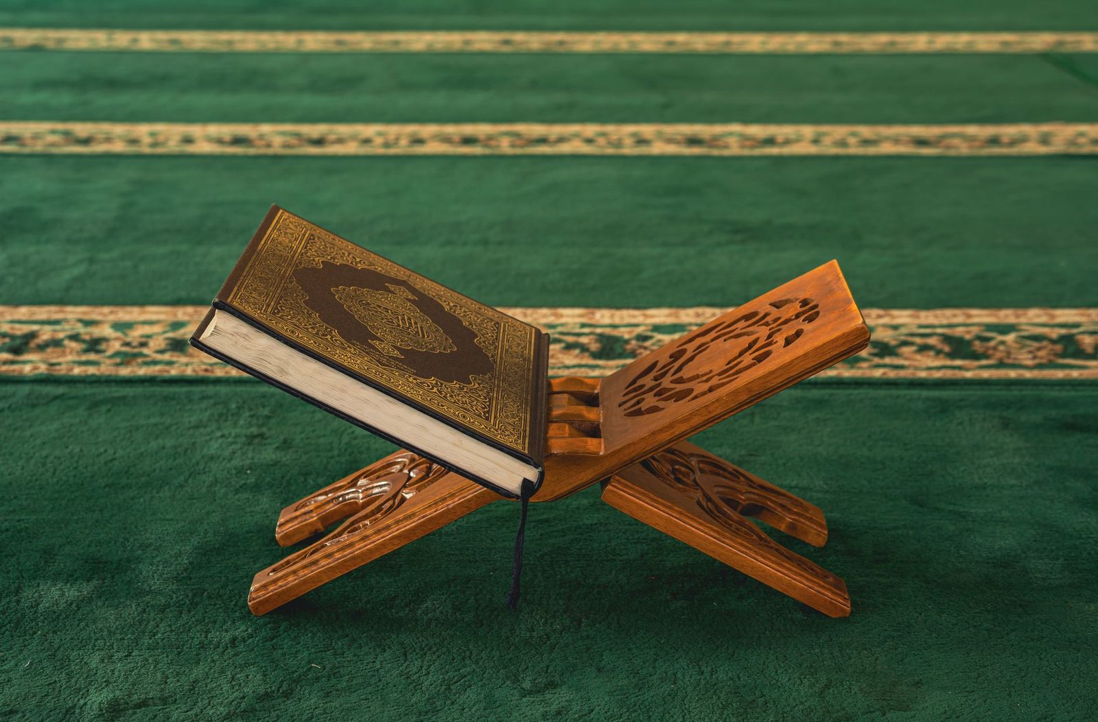 Yeşil cami halısı üzerinde oymalı ahşap rahlede duran kapalı Kur'an-ı Kerim