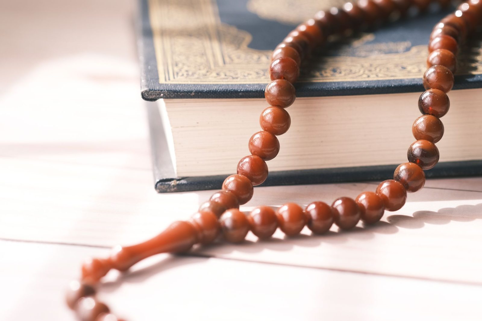 Kapalı bir kitabın üzerine bırakılmış ahşap tesbih; pencereden gelen yumuşak ışık