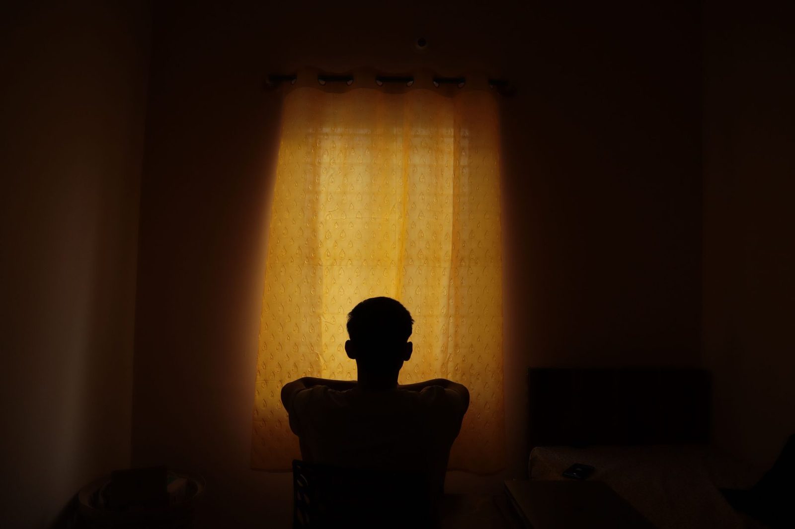 Gece yarısı perdeden süzülen sarı ışığın önünde tek başına oturan bir kişinin karaltısı; ağrının akşam ağırlaşmasının sade temsili