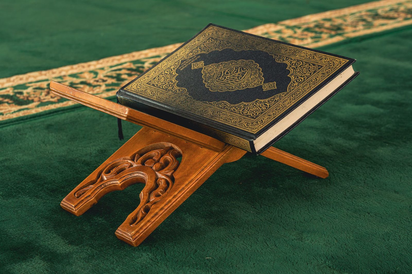 Yeşil cami halısı üzerinde oymalı ahşap rahlede duran kapalı Kur'an-ı Kerim