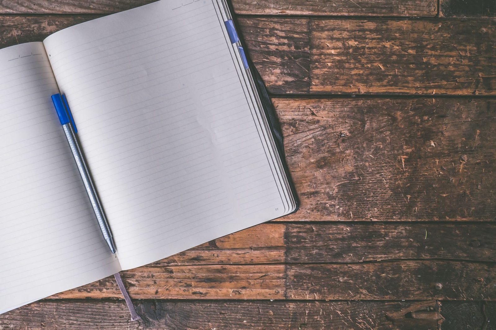 Eski ahşap masa üzerinde açık duran boş çizgili defter ve mavi kalem
