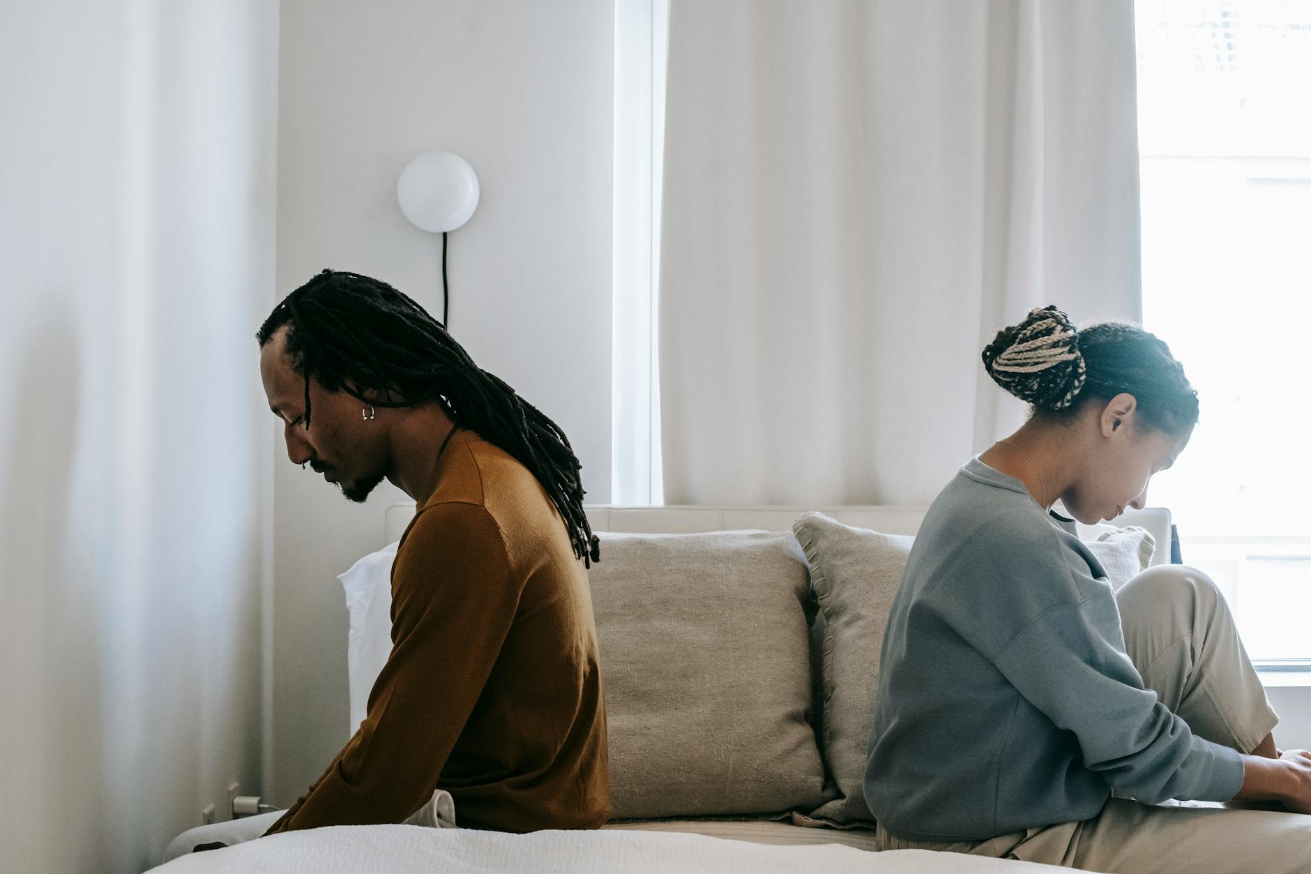 A couple sitting apart in tension — the same wound arriving in a new relationship