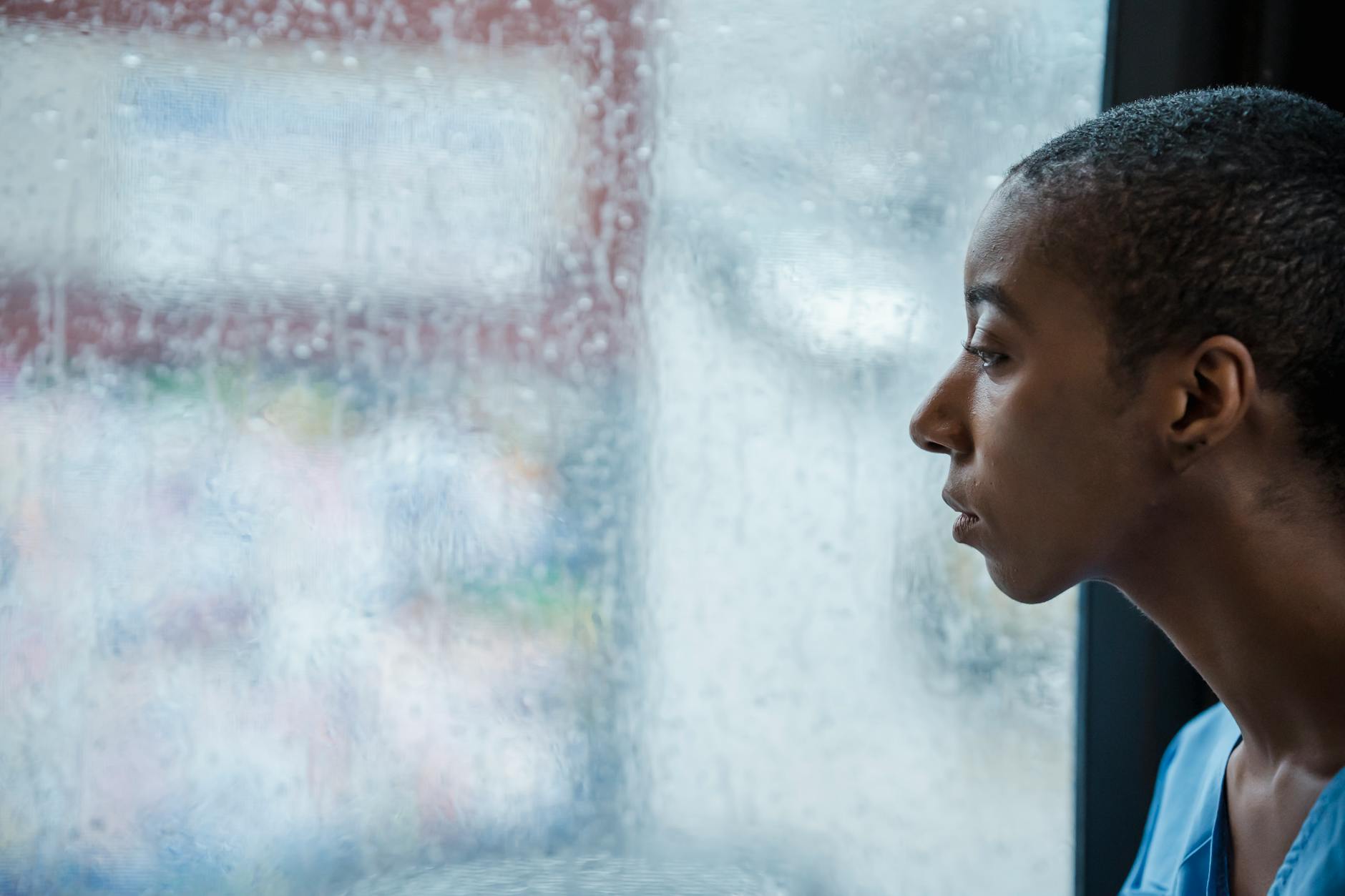 Breaking the pattern — a person alone by a rainy window, the invisible tie still pulling after separation