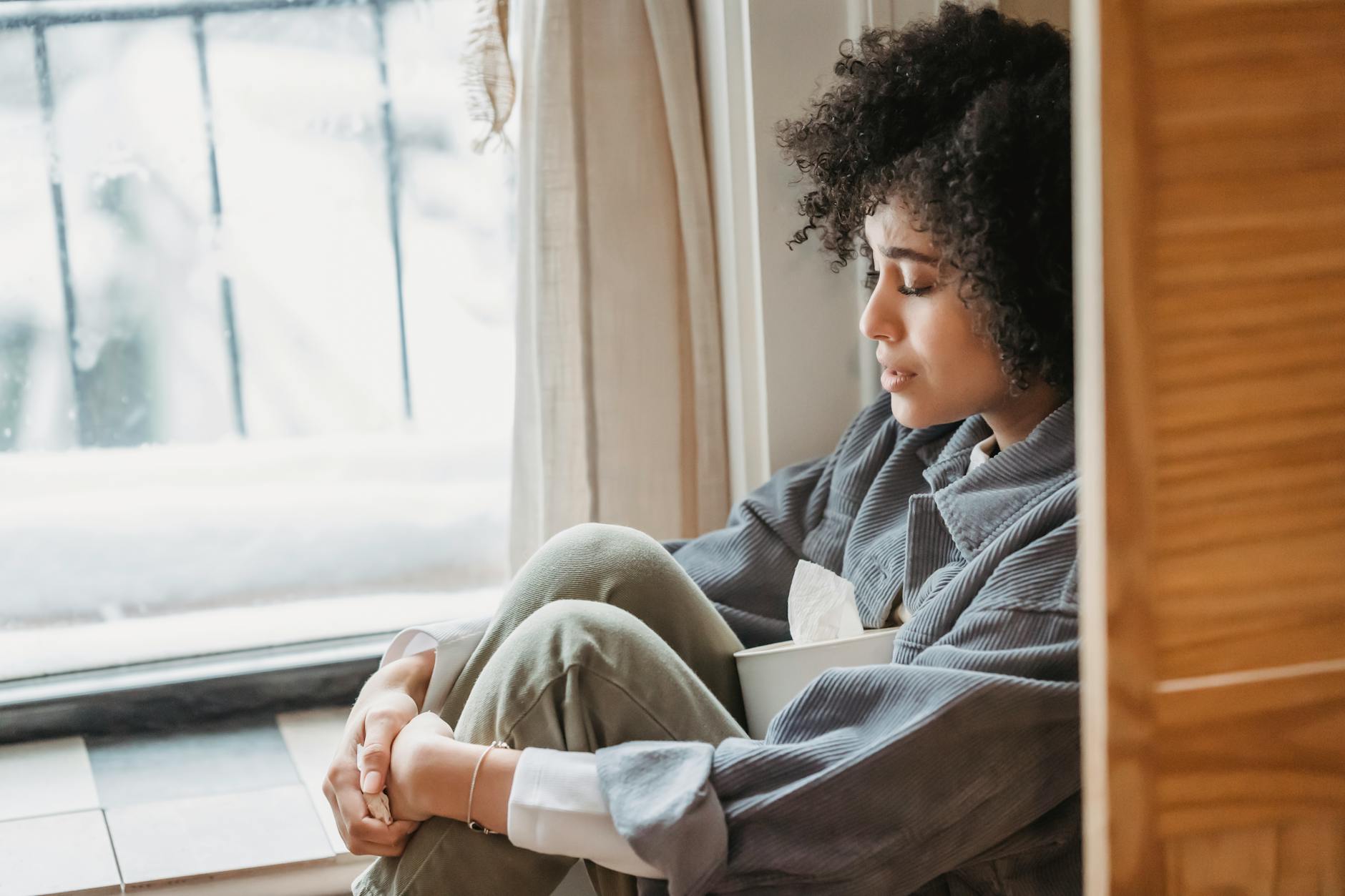 A person sitting alone with knees drawn in — carried charge that lingers long after a relationship ends