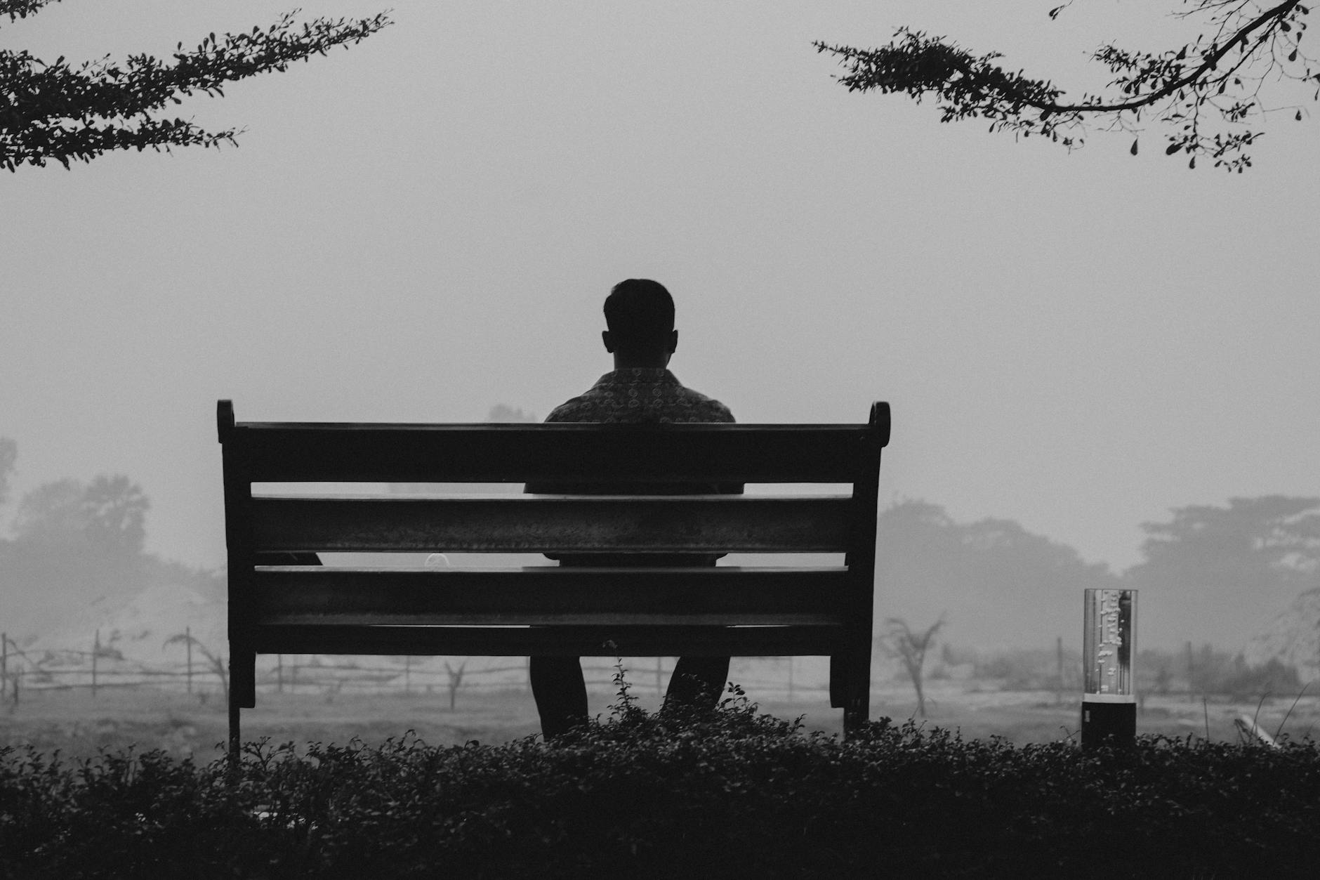A person sitting alone on a bench, the isolation a repeating pattern produces