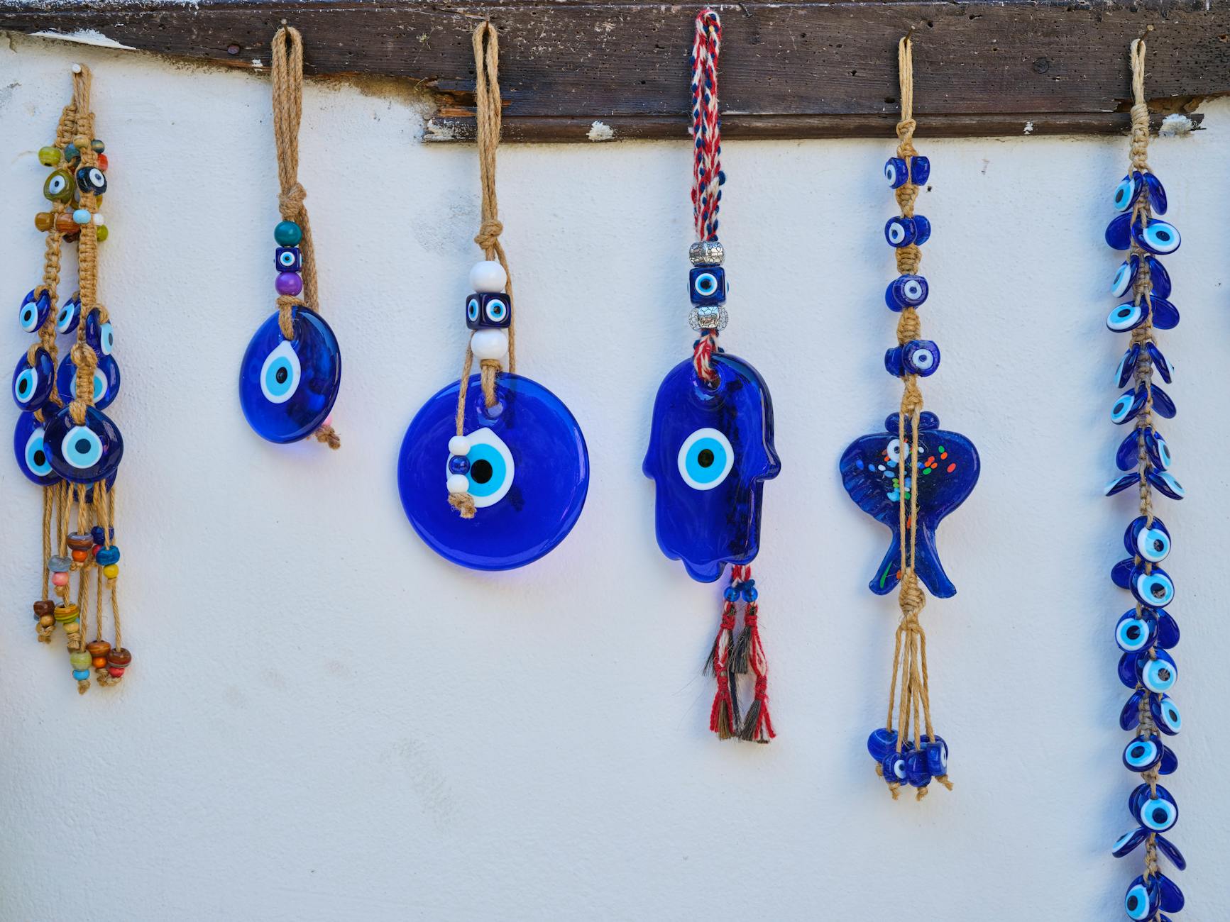 Blue glass evil-eye amulets hanging in clustered rows against a pale wall, used as protection charms in many cultures