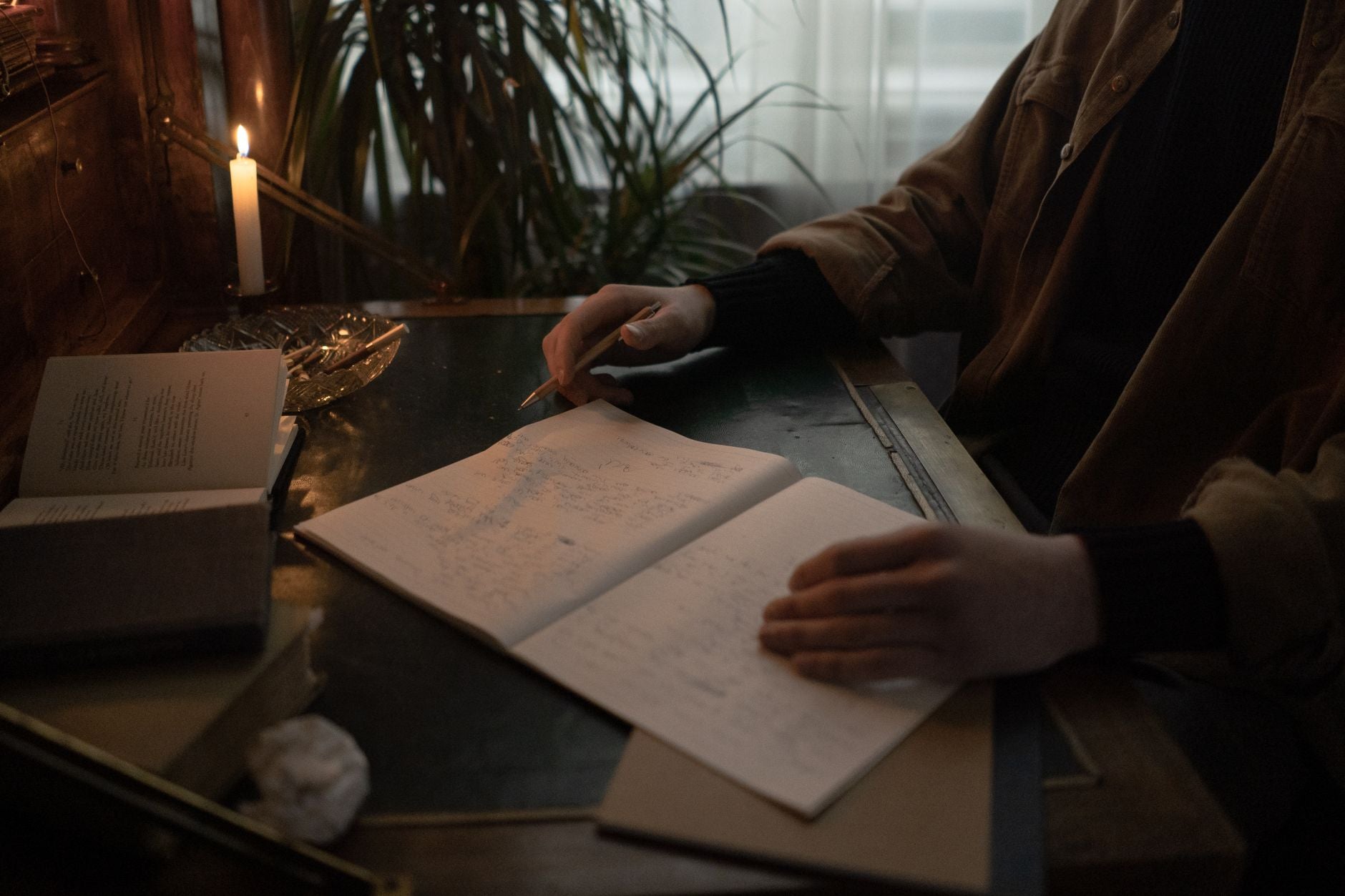 A practitioner at a desk, reviewing handwritten notes by candlelight — the inward, retrospective Mercury current put to deliberate use.