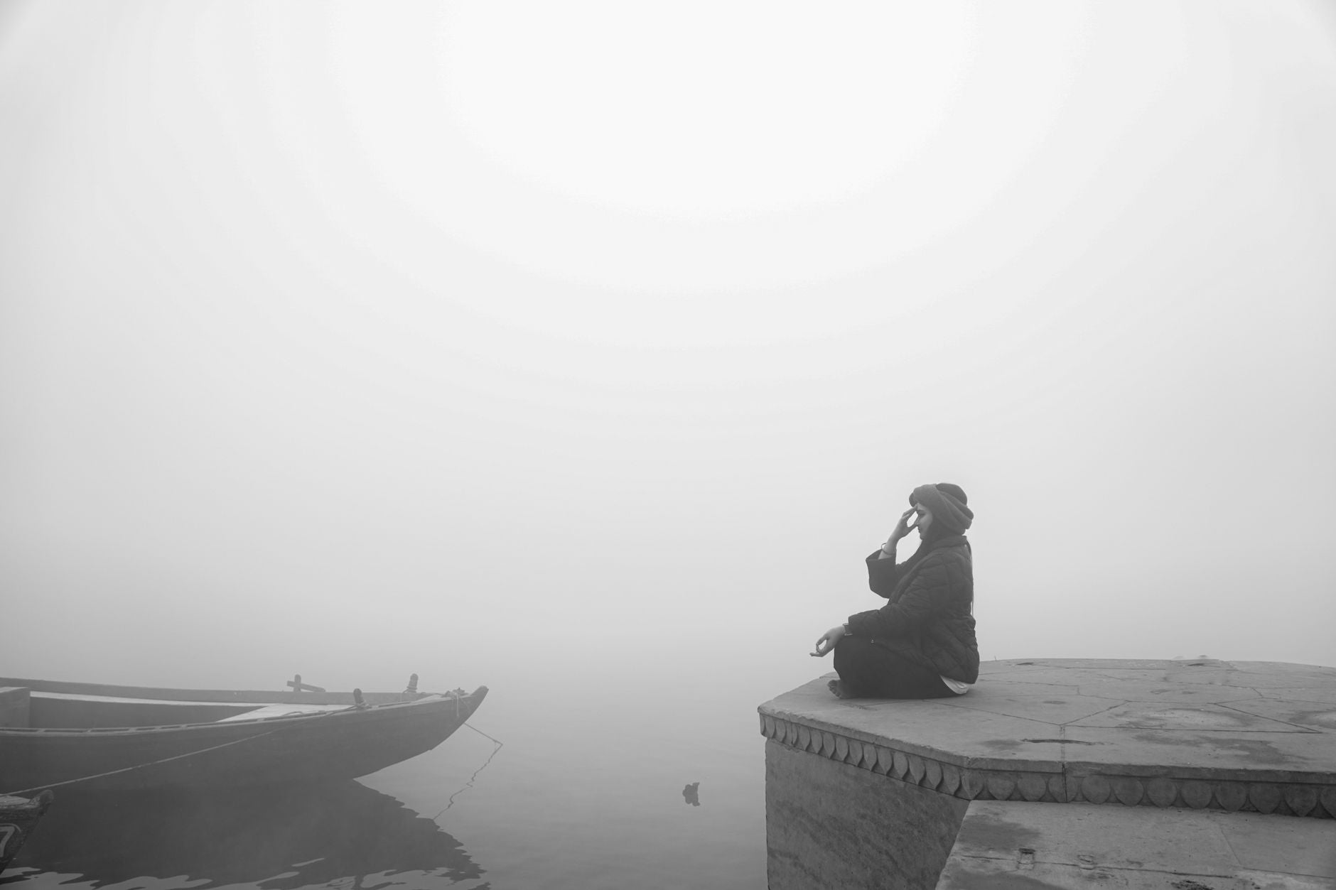 Person seated still on a dock above calm misty water at dawn, stillness while tides move below
