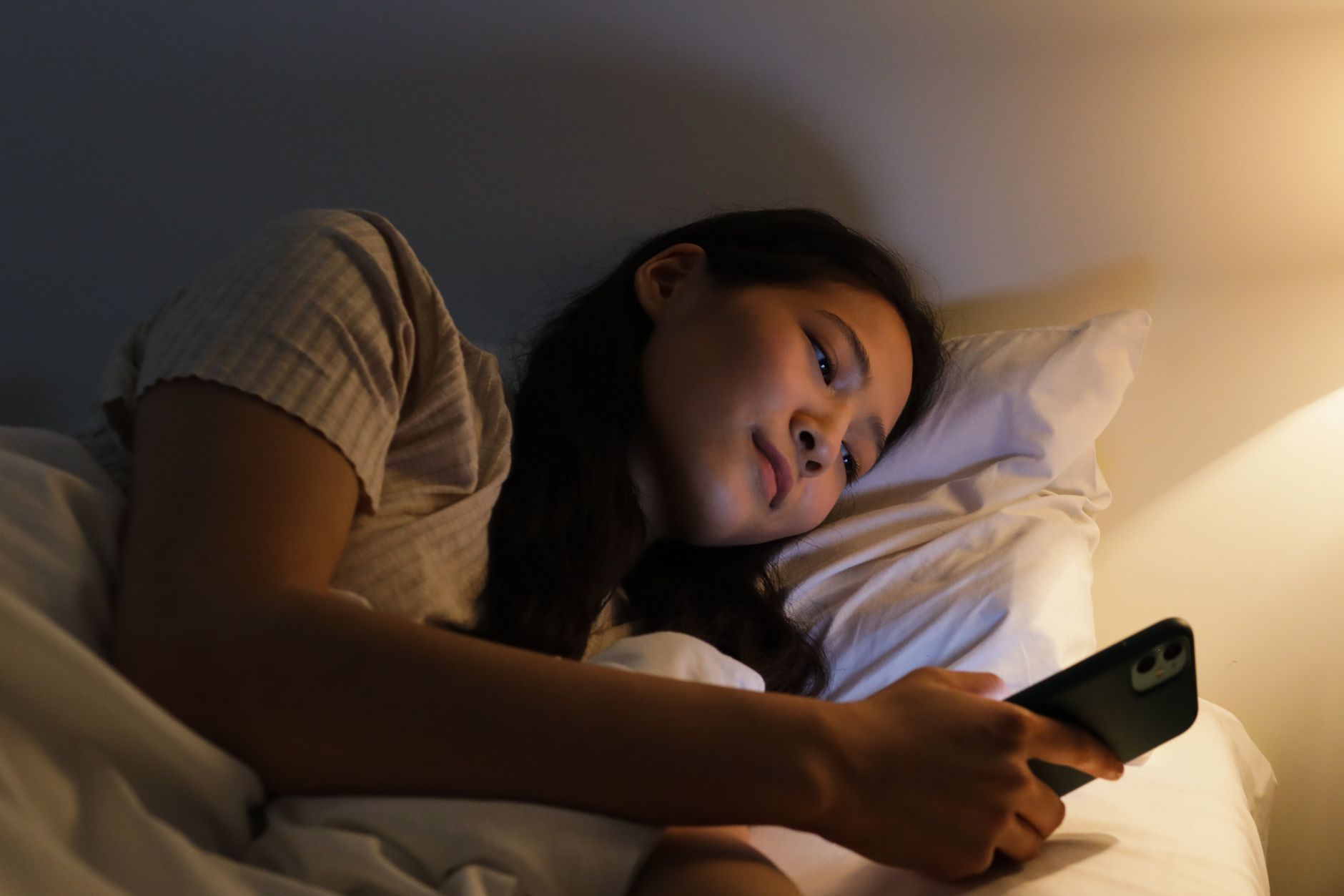 Person lying in bed using a smartphone, lit by warm bedside lighting — the attention economy at work